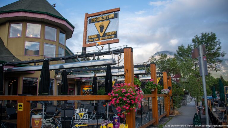 The Grizzly Paw sign rises above a timber patio lined with flower baskets and umbrellas.