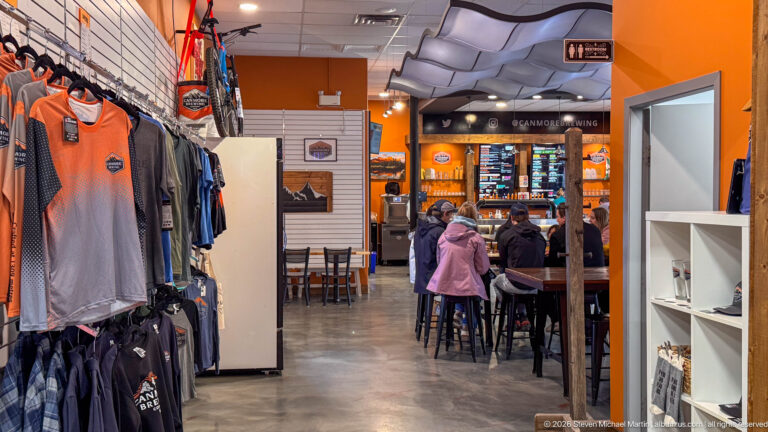 Visitors browse branded brewery shirts beside the service counter inside Canmore Brewing Company.