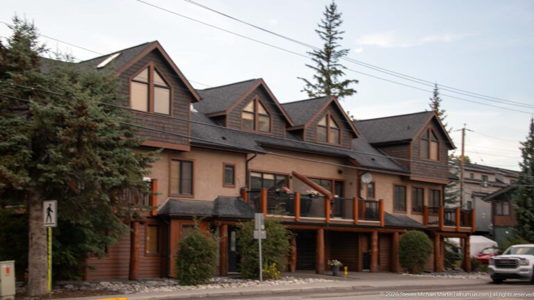 A multi-story condominium with repeated timber gables and balconies fills a Canmore streetscape.