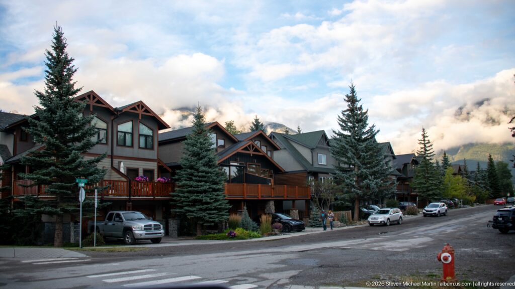 Lodge-style homes with timber gables and balconies line a Canmore street beneath clouded mountains.
