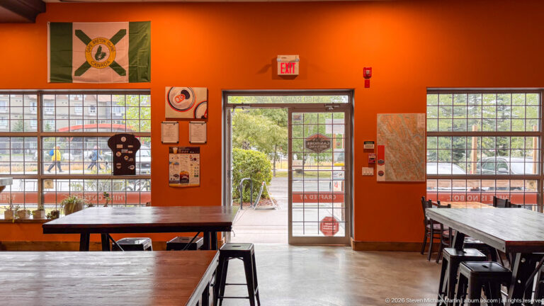 Wooden tables and black stools fill an orange-walled taproom with large street-facing windows.