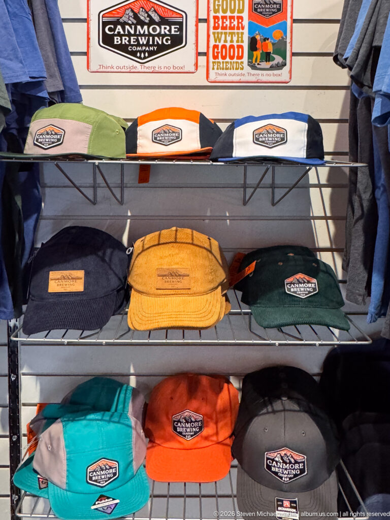 Colorful Canmore Brewing Company caps line a wire shelf beneath branded signs.