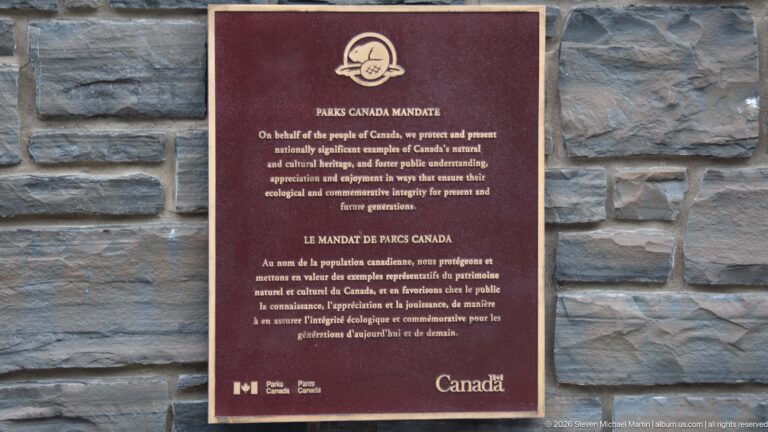 Bilingual Parks Canada mandate plaque with beaver emblem mounted on a gray stone wall.
