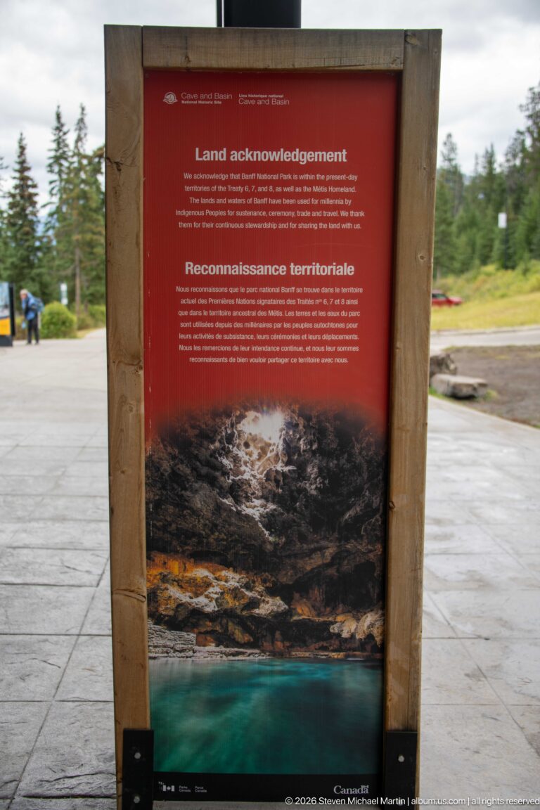 Red bilingual land acknowledgement panel in a timber frame beside the outdoor visitor approach.