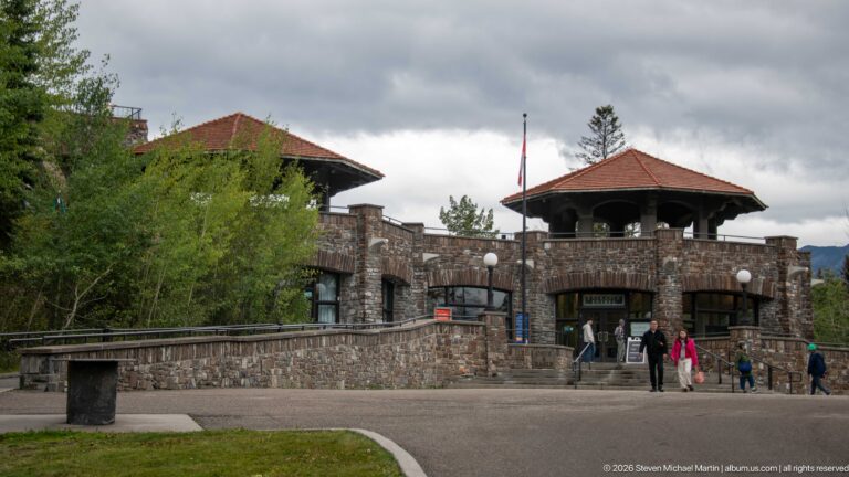 Wide plaza view of the stone entrance building, with visitors approaching its central doorway.