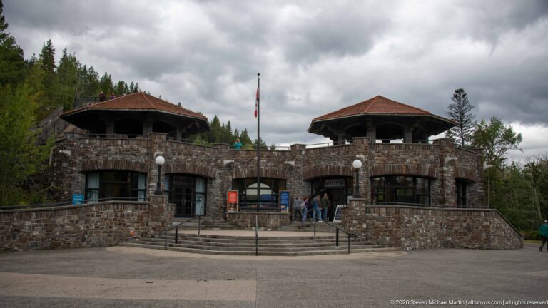 Symmetrical stone entrance building with two raised hipped-roof pavilions, central steps, and visitors.