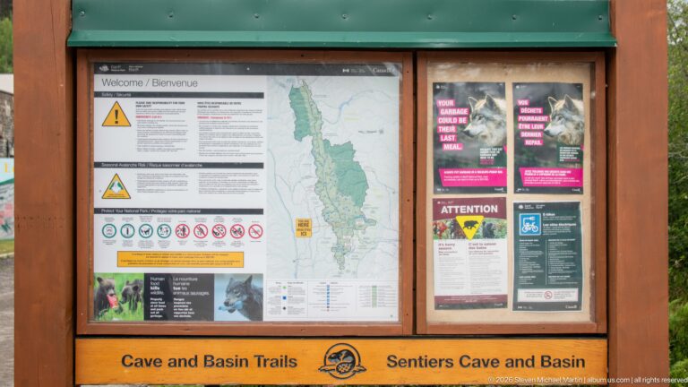 A Cave and Basin Trails kiosk displays a map, safety symbols, and visitor notices.