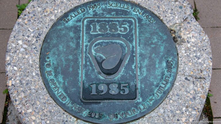 A weathered round medallion marked 1885 and 1985 is embedded in concrete paving.