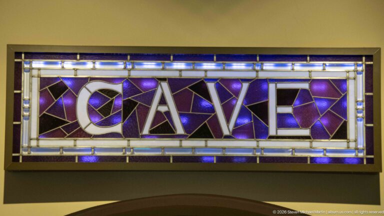 Large pale letters spelling CAVE sit within a purple and blue stained-glass panel.