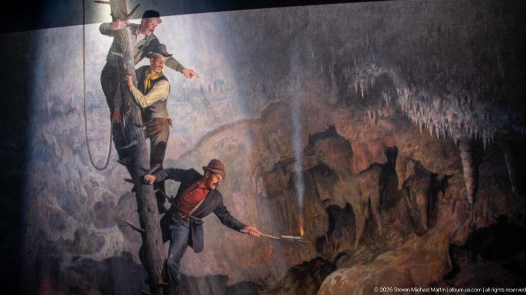 Three men descend by rope along a shadowed rock face in a cave mural.