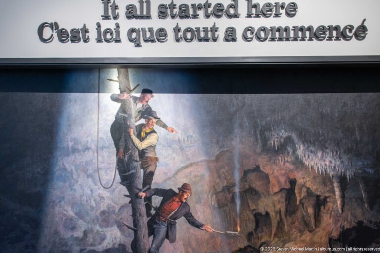 A mural shows three men descending by rope into a cave beneath the words “It all started here.”
