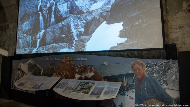 A projected waterfall and a woman’s portrait rise above a curved park-history display.