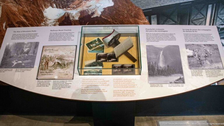 A glass case of printed objects sits among photographs and text on a park-history panel.