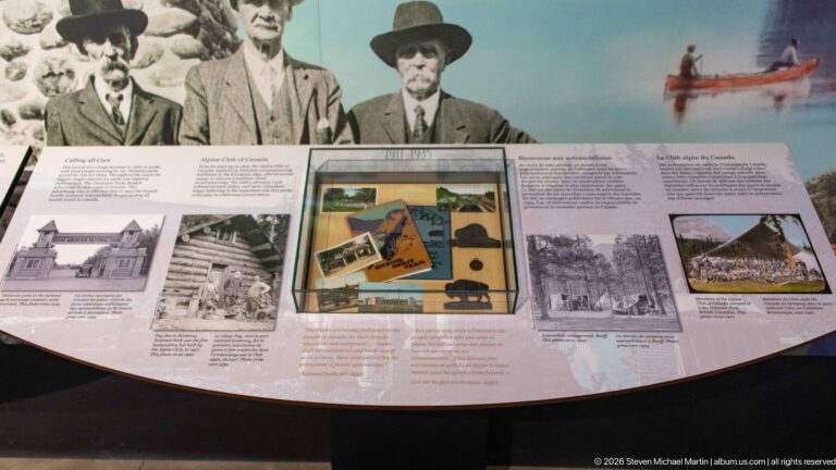 Historic portraits and building photographs surround a glass case of objects in a Banff exhibit.