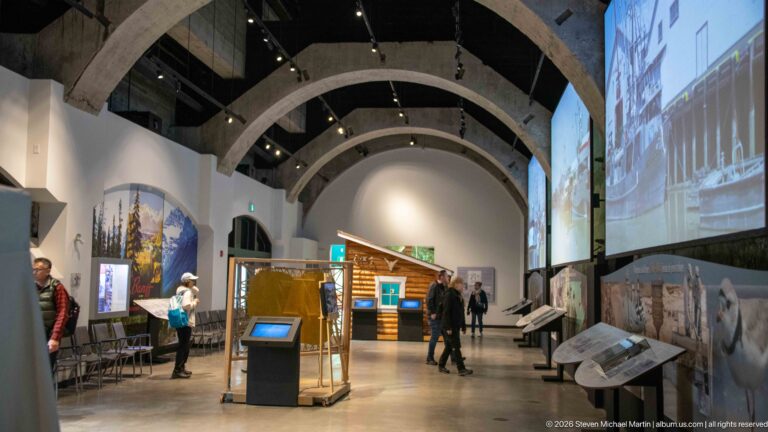 Several visitors explore exhibits beneath repeated stone arches in a vaulted gallery.