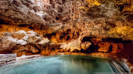 Amber-lit limestone formations overhang a turquoise pool beside a low stone walkway.