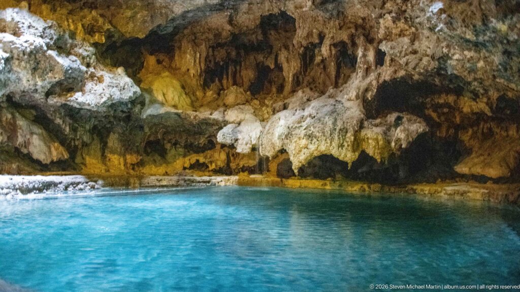 A turquoise pool beneath a low limestone ceiling with irregular mineral formations.