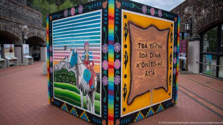 A painted figure on horseback and large Indigenous-language lettering cover adjacent faces of a display cube.