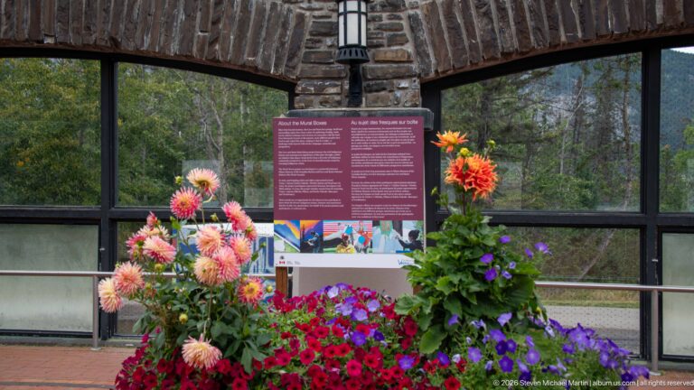 Pink and orange flowers frame a magenta interpretive panel beneath a stone arch.