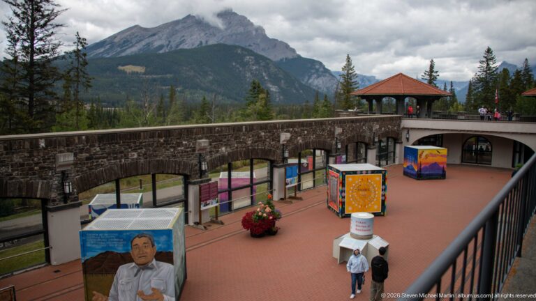 Colorful exhibit panels and display cases stand across the red-paved courtyard beneath stone arches.