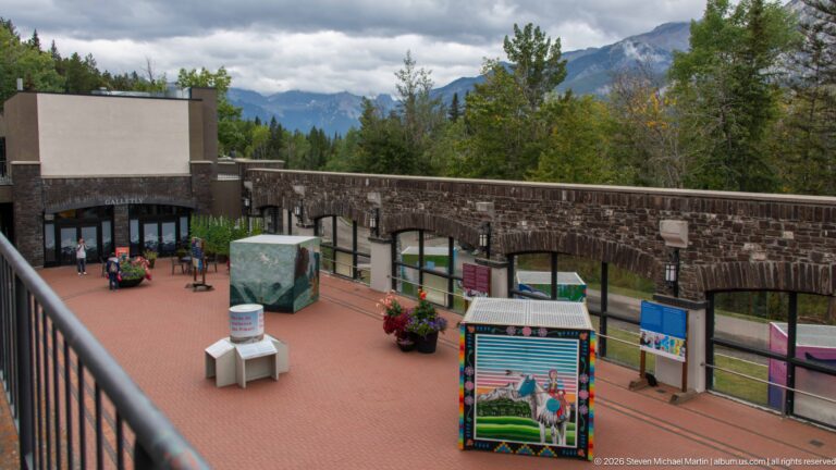 Interpretive panels and display cases fill a paved courtyard beneath a stone arcade.