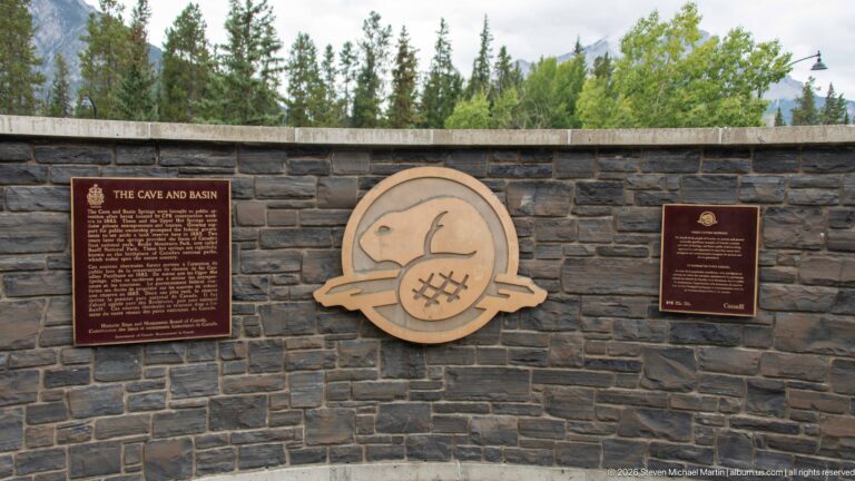 Curved masonry wall with two historical plaques and a large central Parks Canada emblem.
