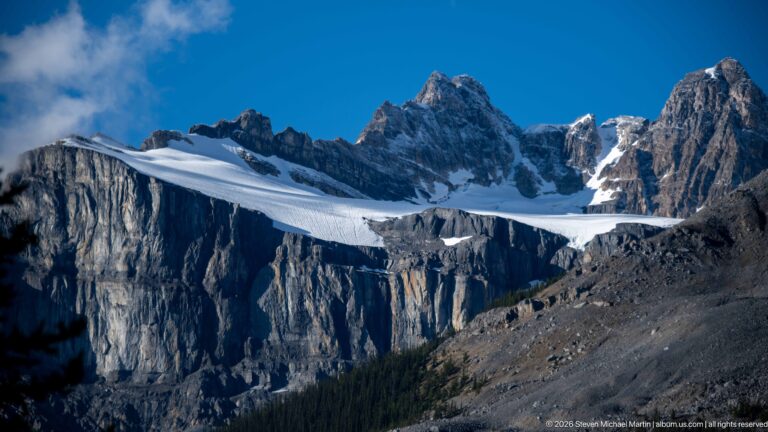 A wide glacier spans a steep basin beneath jagged peaks, above dark cliffs and moraine.