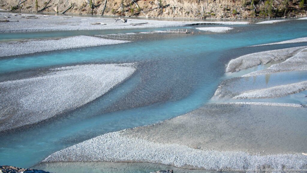 Turquoise channels split around pale gravel bars in a broad braided riverbed.