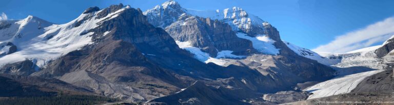 Jagged snowy peaks rise above a fractured glacier descending between dark mountain slopes.