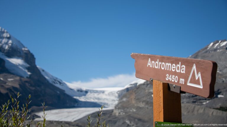 A brown sign reading “Andromeda 3450 m” stands before a softly focused glacier.