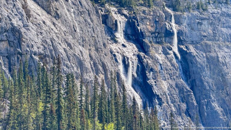 A bright waterfall drops through a narrow cleft in a dark groove of pale limestone.