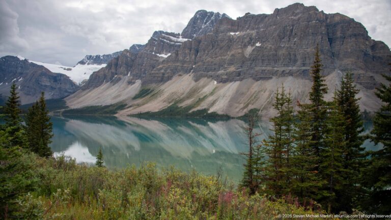 A glacier descends between rocky peaks toward a blue-green lake bordered by conifers.