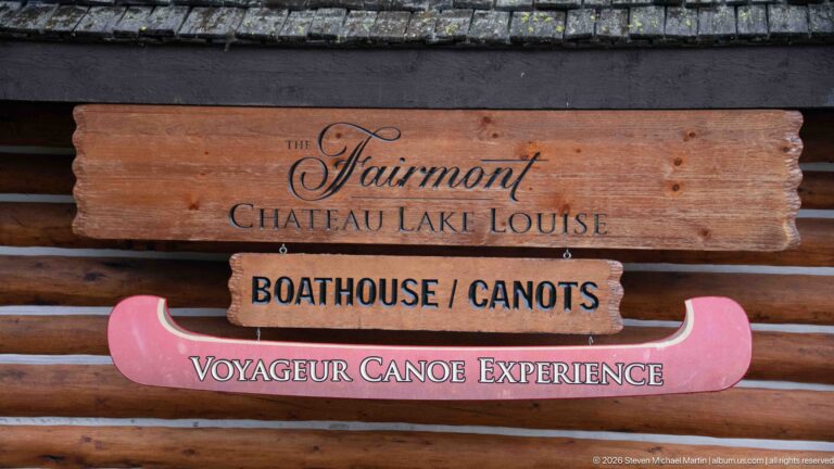 A wooden sign on a log wall names the Fairmont Chateau Lake Louise boathouse and Voyageur Canoe Experience.