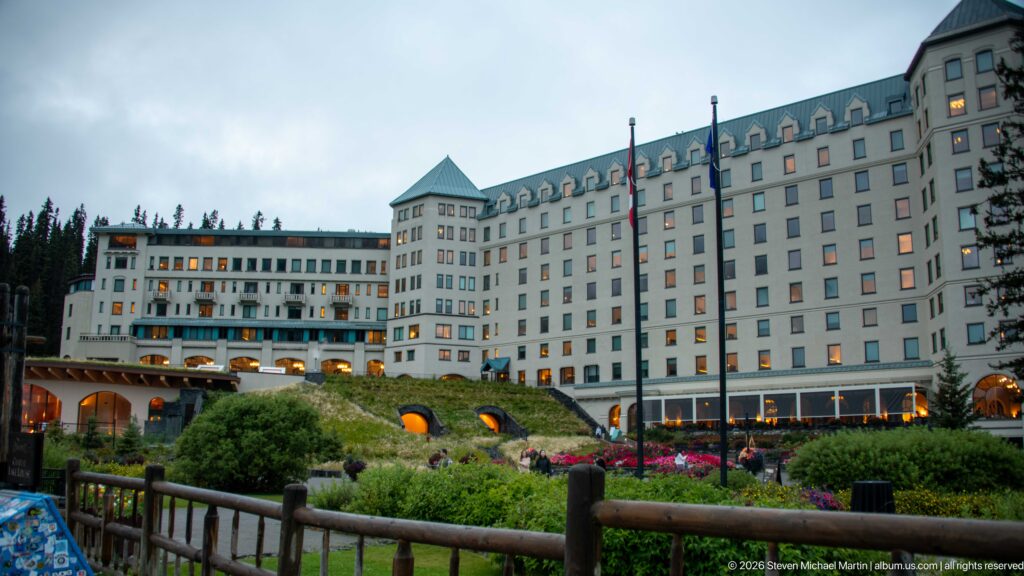 The Fairmont Chateau Lake Louise rises above flower beds and a timber-railed garden path.