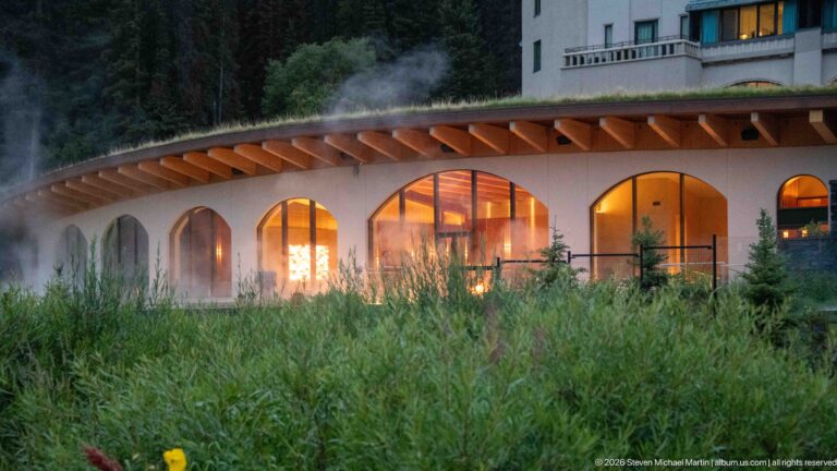 Warm light glows through arched doors beneath the broad roof overhang of the Fairmont Chateau Lake Louise.
