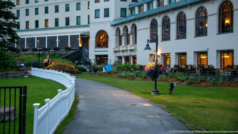 A white-railed path curves through flower beds beside the arched windows of the Fairmont Chateau Lake Louise.