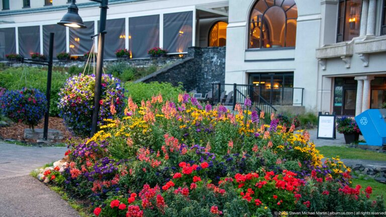 A curved bed of colorful flowers borders a walkway beside the Fairmont Chateau Lake Louise’s tall windows.