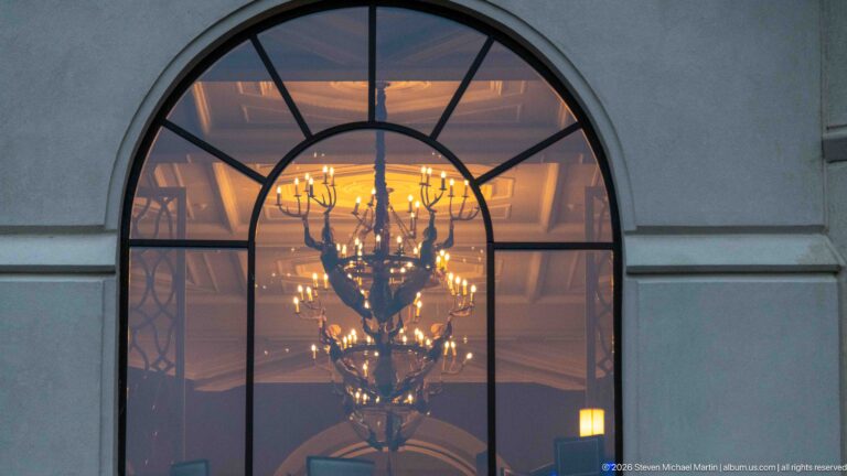 A multi-tier chandelier glows behind the muntins of a large arched window at the Fairmont Chateau Lake Louise.