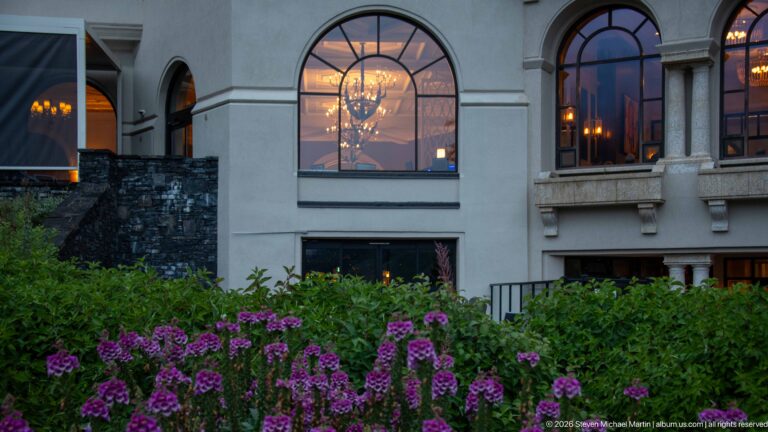 Purple shrubs grow beneath tall arched windows in the pale stone façade of the Fairmont Chateau Lake Louise.