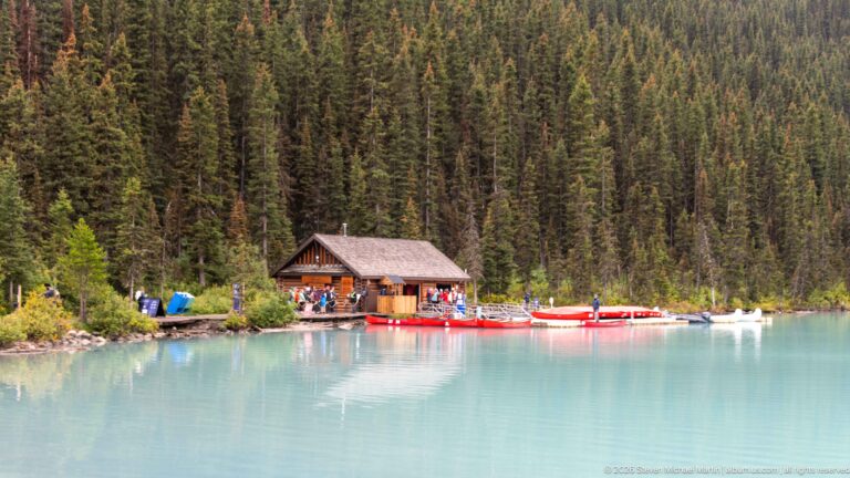 Red rental canoes line the shore beside a log boathouse on Lake Louise.