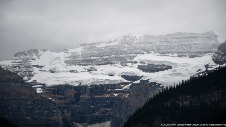 Victoria Glacier fills a broad mountain basin beneath layered peaks and above dark forest slopes.