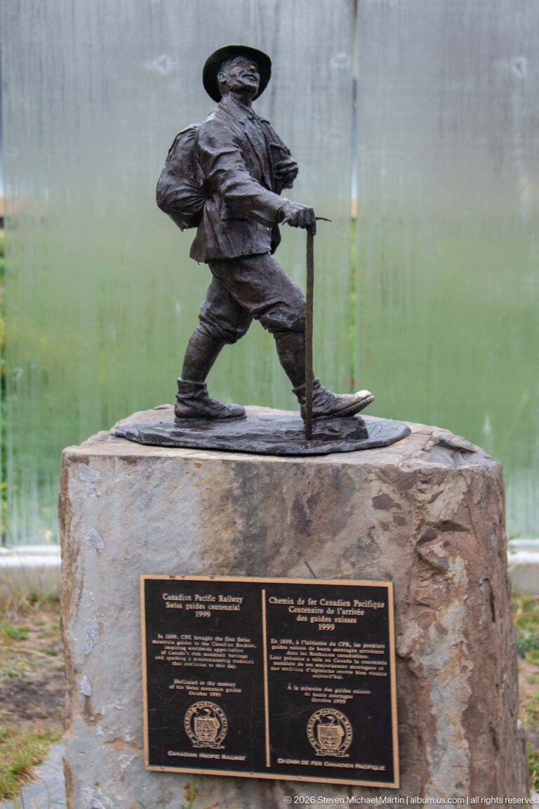 A bronze mountaineer stands on a stone plinth above two bilingual plaques.