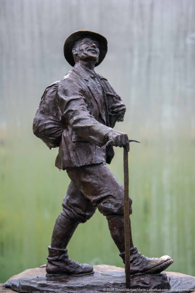A bronze mountaineer in a broad-brimmed hat holds a long staff or ice axe.