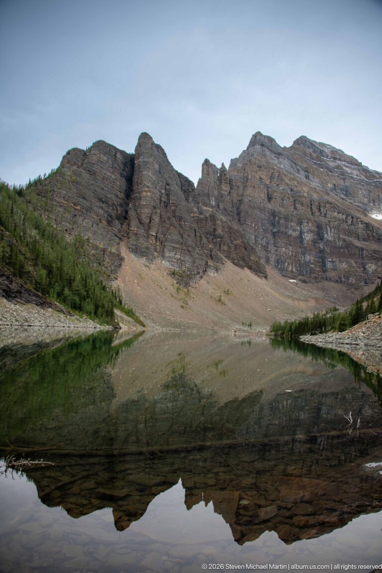 A broad layered ridge and its reflection fill the view across Lake Agnes.