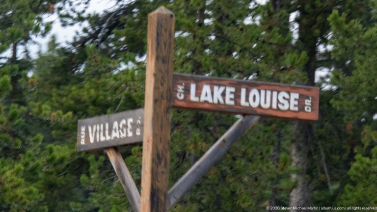 A wooden sign points toward Lake Louise, with a partly cropped directional board below it.