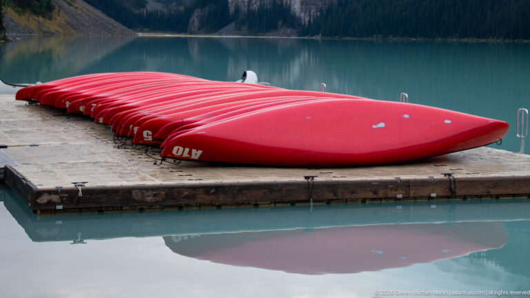 Red rental canoes rest upside down on a floating dock, reflected in Lake Louise.
