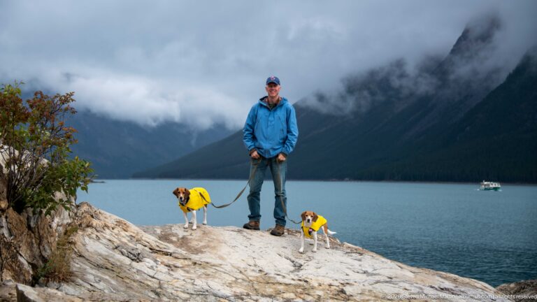 Man and two beagles on a rocky point above Lake Minnewanka with a distant boat.