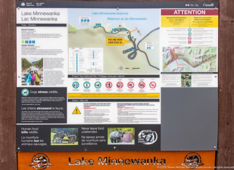 Lake Minnewanka information board displaying a reservoir map, safety notices, regulations, and wildlife guidance.