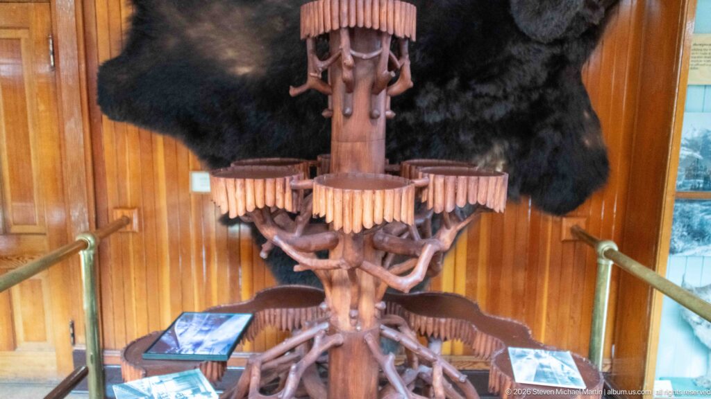 Large multi-tiered rustic wooden fixture made from branching limbs inside the wood-paneled museum.