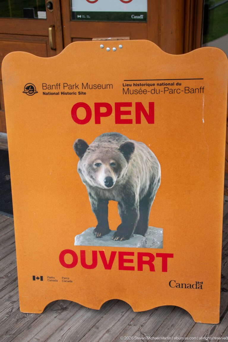 Orange Banff Park Museum sign reading OPEN and OUVERT with a bear illustration and Parks Canada branding.